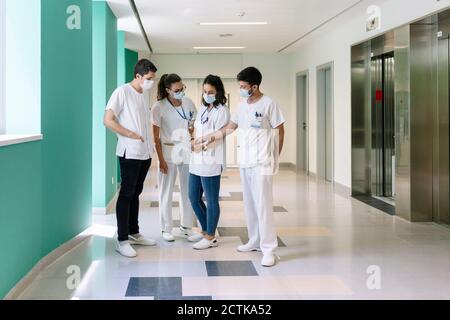 Les médecins portant des masques chirurgicaux discutant au-dessus d'une tablette numérique debout dans un couloir à l'hôpital Banque D'Images