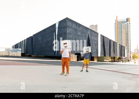Les garçons portant des masques robotisés se tenant sur la route contre la construction ville Banque D'Images