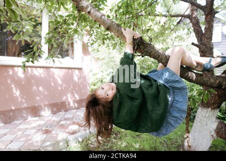 Jolie fille accrochée à la branche de l'arbre dans la cour arrière Banque D'Images