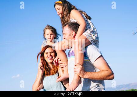 Parents joyeux portant des filles sur les épaules contre le ciel clair pendant jour ensoleillé Banque D'Images