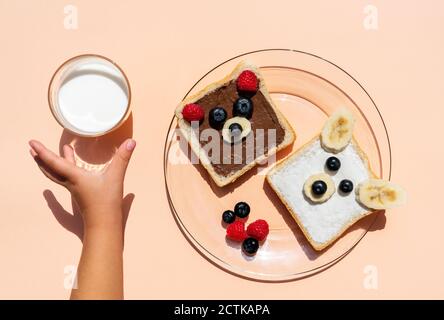 Studio de toasts avec des visages d'ours faits de fruits et main de bébé fille atteignant pour un verre de lait Banque D'Images