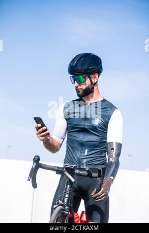 Cycliste masculin utilisant un smartphone en étant debout avec un vélo contre le ciel dégagé Banque D'Images