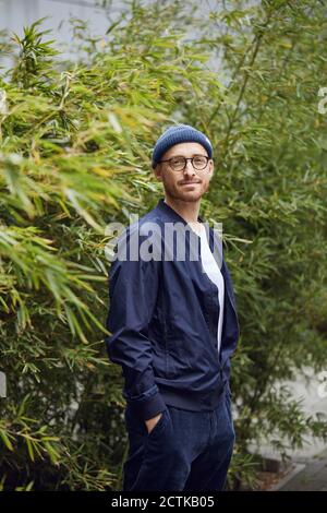 Homme adulte moyen debout avec les mains dans les poches contre le vert feuilles Banque D'Images