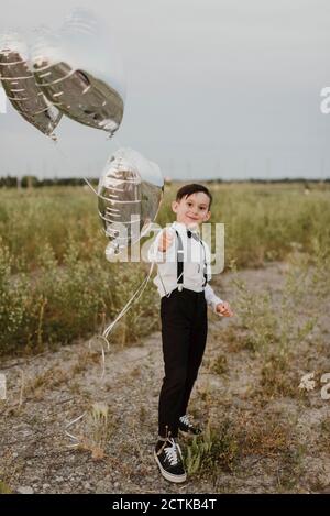 Garçon avec des ballons en forme de coeur debout dans le champ contre clair ciel Banque D'Images