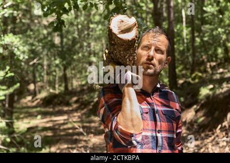 Homme de bois attentionné portant une bûche sur l'épaule tout en regardant loin forêt Banque D'Images