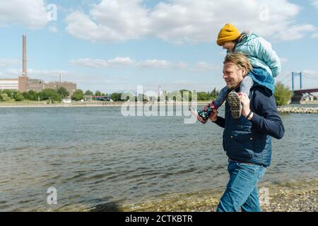 Père portant sa fille sur l'épaule tout en marchant près de la rive de la rivière Banque D'Images