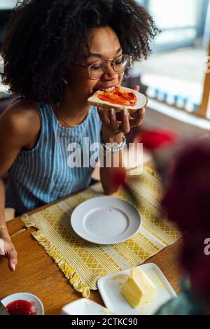 Jeune femme avec les yeux fermés manger du pain tout en s'asseyant à tableau Banque D'Images