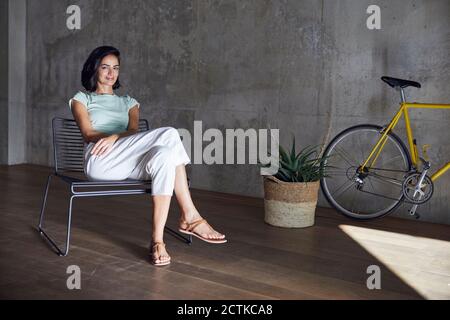 Femme d'affaires souriante se détendant sur une chaise à l'usine et à vélo bureau Banque D'Images