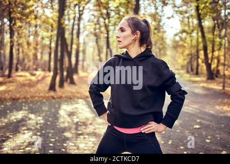 Jeune femme jogger pendant la pause regardant latéralement dans la forêt d'automne Banque D'Images