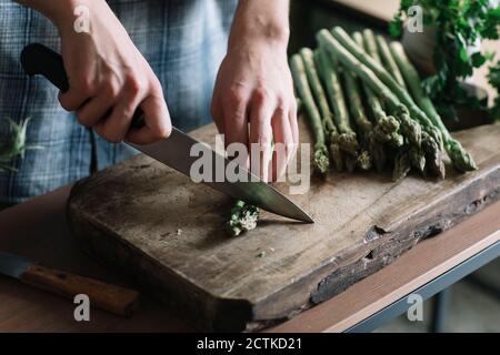 Mains de l'homme coupant des asperges fraîches à bord dans la cuisine Banque D'Images