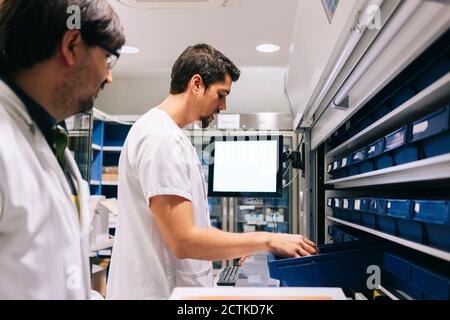 Homme mature debout avec un collègue qui vérifie les médicaments dans l'étagère à pharmacie Banque D'Images