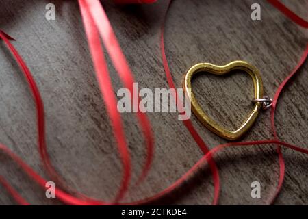 Coeur en acier doré avec quelques rubans rouges sur un bois tableau Banque D'Images