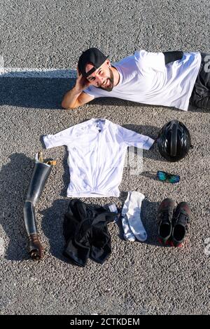 Athlète masculin souriant amputé avec divers objets couchés sur la route Banque D'Images