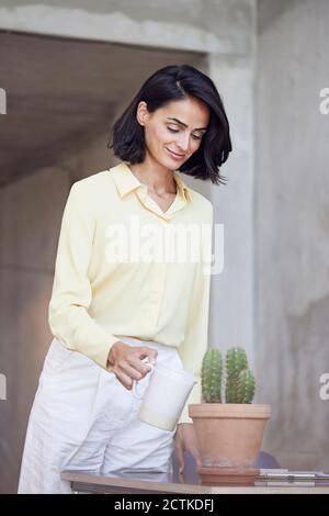 Femme d'affaires souriante qui arrose des plantes de cactus sur le bureau Banque D'Images