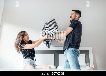 Couple heureux ayant un combat d'oreiller sur le lit dans la chambre Banque D'Images