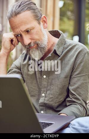 Gros plan sur un homme mûr mûr et mûr, bien pensé, assis sur un ordinateur portable dans la cour Banque D'Images