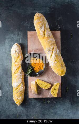 Planche à découper, baguettes fraîches et bol avec curcuma et romarin Banque D'Images