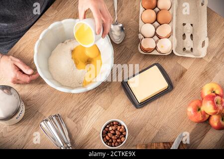 Femme à la main mettant le jaune d'œuf dans un bol tout en se tenant à îlot de cuisine Banque D'Images