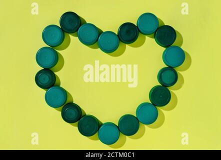 Bouchons de bouteille en plastique vert formant un cœur sur fond jaune Banque D'Images