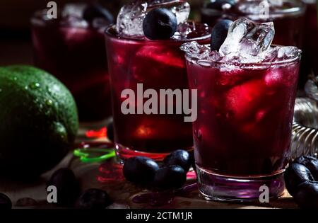 Cocktail alcoolisé avec liqueur, bleuet, jus de lime, glace pilée, outils de bar sur fond noir, attention sélective Banque D'Images