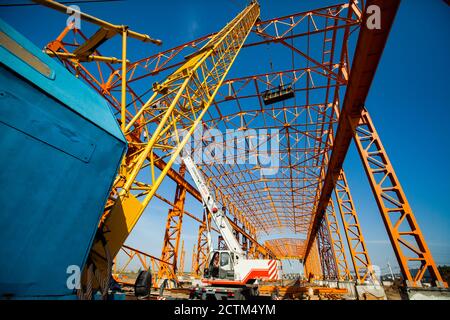 Kostanay/Kazakhstan - Mai 14 2012: Construction d'une nouvelle usine de construction structure en acier orange. Grue à poutre jaune et travailleurs en suspension de construction Banque D'Images