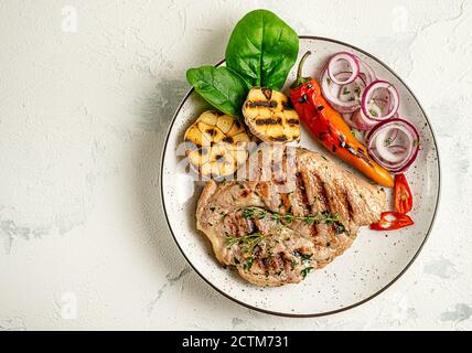 Assiette de steak de porc grillé avec légumes sur fond de béton. Concept de régime cétogène. Surcharge, espace de copie. Banque D'Images