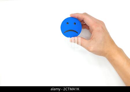 Main tenant une icône de visage triste bleu sur fond blanc avec espace de copie. Notion de tristesse et de solitude. Banque D'Images