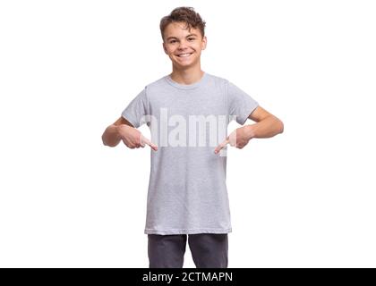 Jeune garçon souriant, isolé sur fond blanc. Un enfant heureux pointe ses doigts sur un t-shirt vierge. Banque D'Images