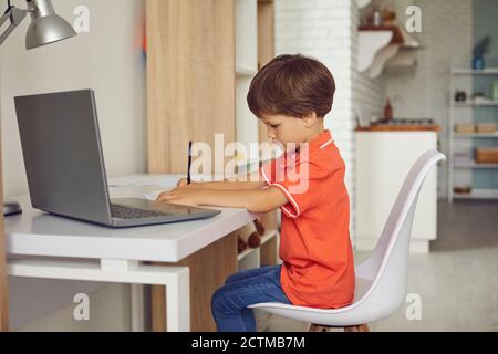 Un garçon concentré qui fait ses devoirs à l'aide d'un ordinateur portable moderne bureau à la maison Banque D'Images