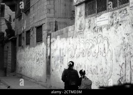 Deux écolières palestiniennes marchant le long d'un mur couvert de graffitis sur le chemin de l'école dans la ville de Gaza Palestine mars 2008 Banque D'Images