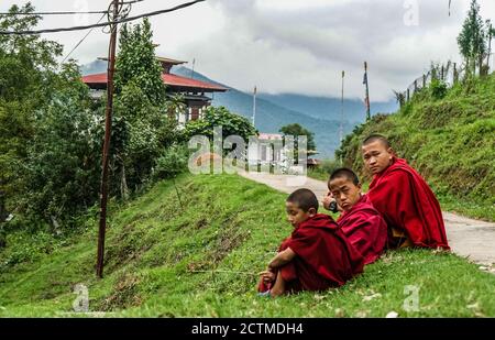Trois moines enfants assis près de la route à Punakha, au Bhoutan Banque D'Images