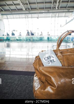 Housse pour sac et passeport avec citation motivationnelle « Explorer » dans un terminal de l'aéroport avec les voyageurs en arrière-plan Banque D'Images