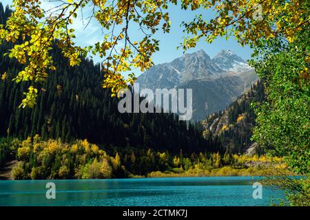 Vue sur le lac de montagne Issyk. Ambiance d'automne. Le lac turquoise est entouré de montagnes avec des arbres à jaunins. Banque D'Images