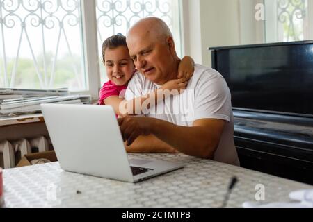 Portrait du grand-père et de la petite-fille faisant leurs devoirs avec un ordinateur portable. Banque D'Images