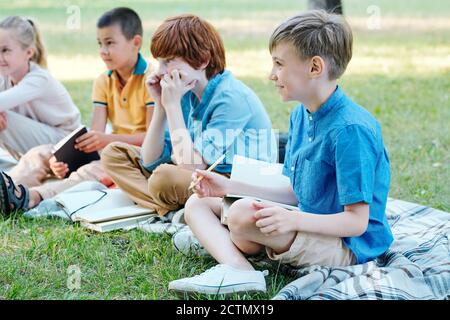 Curieux enfants assis avec des classeurs sur des supports tout en écoutant professeur à la leçon de plein air Banque D'Images