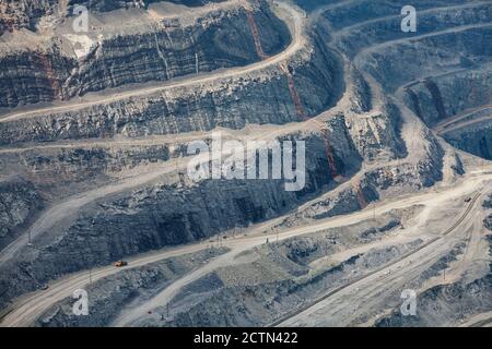 Extraction à ciel ouvert de minéraux bruts pour la production d'acier. Carrière de minerai de fer géant à Rudny, Kazakhstan. Couches géologiques et petit camion de carrière jaune vers le bas. Banque D'Images