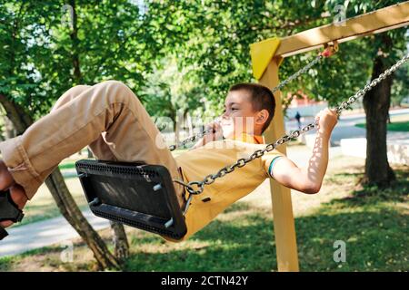 Adorable garçon en chemise jaune s'amusant dans le parc public tout en balançant seul Banque D'Images