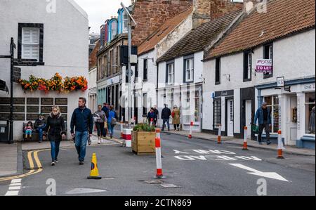 North Berwick, East Lothian, Écosse, Royaume-Uni, 24 septembre 2020. Les mesures d'élargissement de la chaussée pandémique du coronavirus Covid-19 avec des baguettes de route et des jardinières dans l'étroite High Street permettent aux piétons de plus d'espace pour marcher pendant qu'une femme portant un masque facial marche le long de la route Banque D'Images