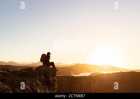 Vue latérale d'un randonneur anonyme avec sac à dos faites du rock dans les montagnes et profitez d'un incroyable coucher de soleil pendant vos vacances Banque D'Images