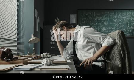 Brillant jeune mathématicien assis au bureau et en examinant ses papiers, il est concentré et d'étudier de nouvelles formules Banque D'Images