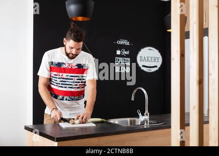 Homme sérieux debout au comptoir à la maison et coupant frais légume pendant la préparation du déjeuner dans la cuisine Banque D'Images