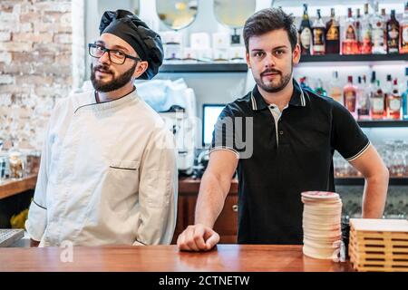 Cuisinier et barman sérieux debout au comptoir dans le bar et regarder l'appareil photo Banque D'Images