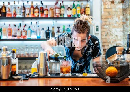 Barman mâle concentré avec des dreadlocks versant de l'alcool dans le verre et préparation d'un délicieux cocktail au comptoir au bar Banque D'Images