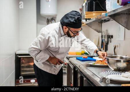 Cuisez les hommes en uniforme, debout au comptoir en métal cuisine de café et préparer un délicieux plat avec du saumon Banque D'Images