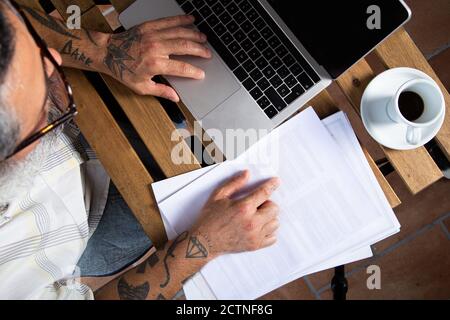 De dessus de la récolte mâle non reconnaissable dans les vêtements décontractés avec bras tatoués qui naviguent sur un ordinateur portable tout en travaillant à distance à la table lieu de travail à domicile Banque D'Images