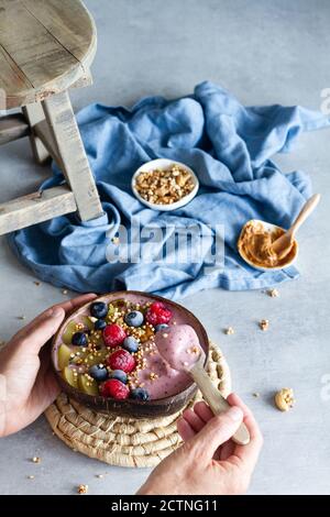 Grand angle de la femme méconnaissable ayant un petit déjeuner savoureux et appréciant bol à smoothie avec yaourt et baies Banque D'Images