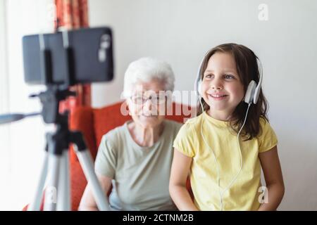 Femme et fille souriante assise dans le salon ensemble et ayant des appels vidéo sur un smartphone Banque D'Images