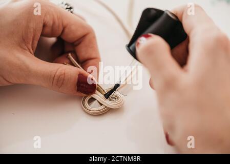 Gros plan à grand angle de la femelle artisanale anonyme encollage des fils tout en faire de la boutache en atelier Banque D'Images