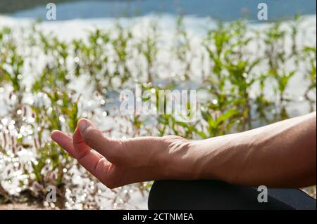 Croisez une femme méconnaissable avec Gyan Mudra gestuelle pratiquant le yoga méditation sur le rivage d'un lac calme dans la nature Banque D'Images