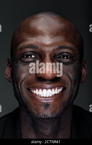 Tête et épaules gros plan portrait d'assurance et de gaieté homme noir afro-américain au visage souriant et expressif sur fond noir Banque D'Images